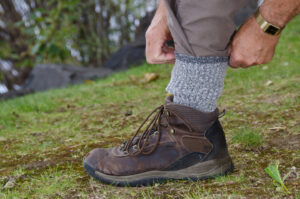 man protecting himself from ticks by using tick repellent, tucking his pant legs into his wool socks, and wearing hiking boots in the woods 